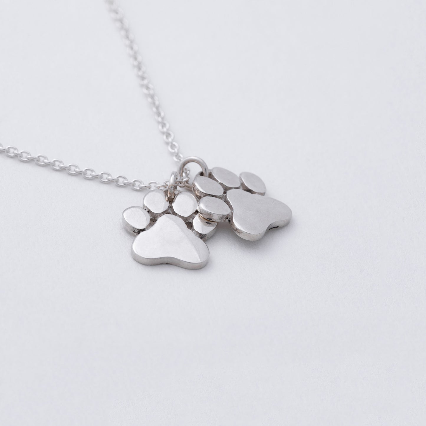 Silver necklace with paw-shaped pendants on a light gray background