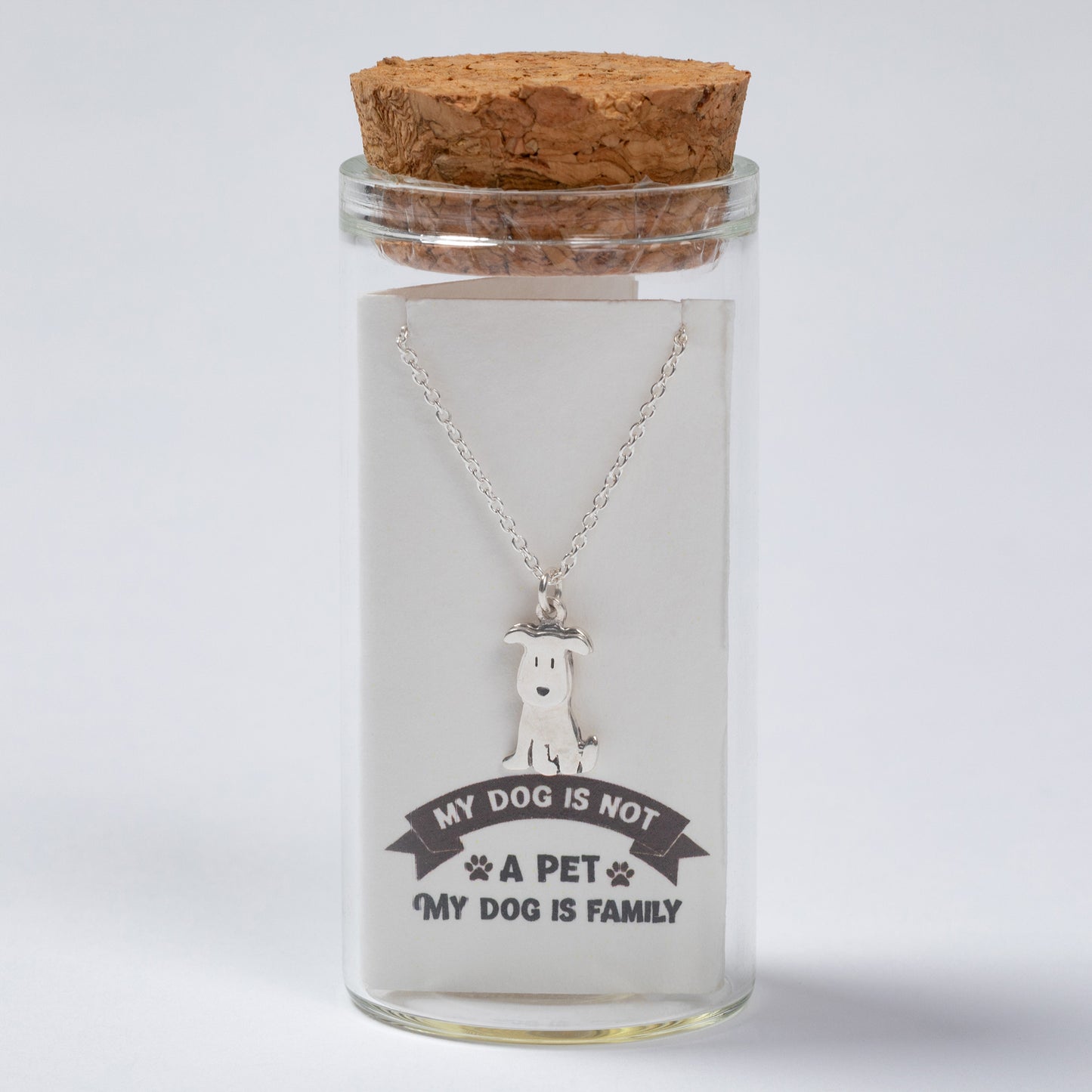 Glass jar with cork lid containing a necklace with a dog pendant and engraved text on a white background