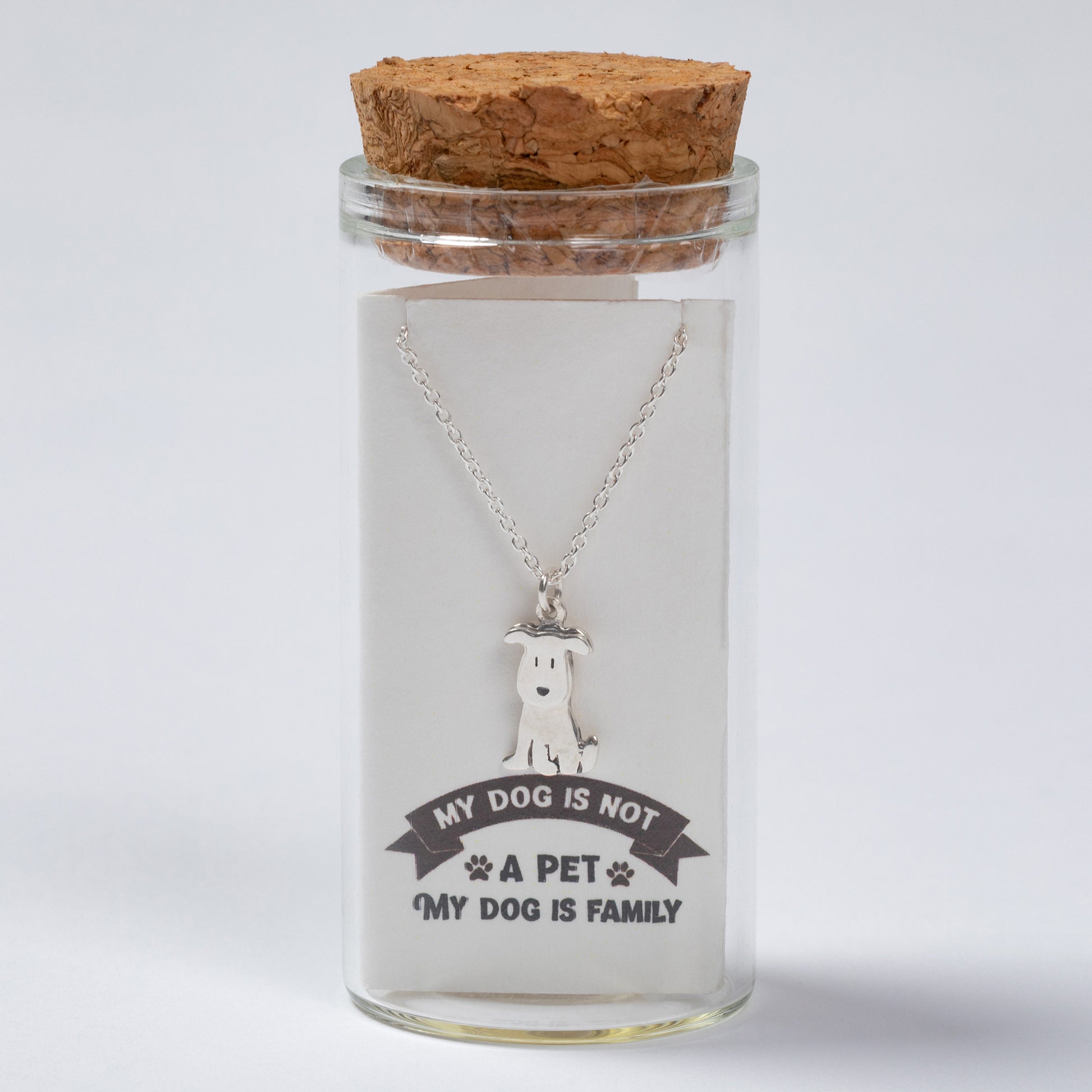 Glass jar with cork lid containing a necklace with a dog pendant and engraved text on a white background