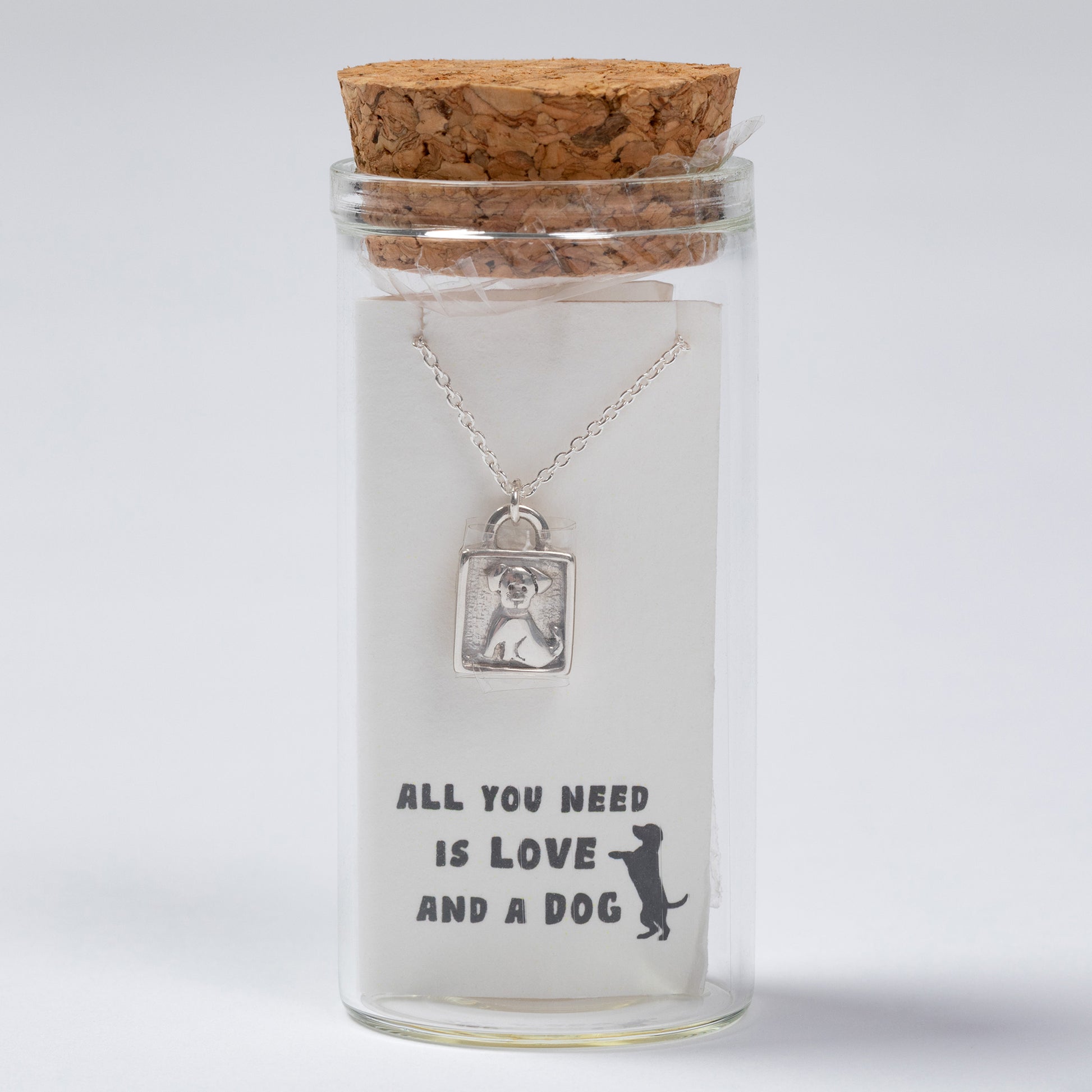 Glass jar with cork lid containing a necklace with a dog pendant and text 'All you need is love and a dog'.