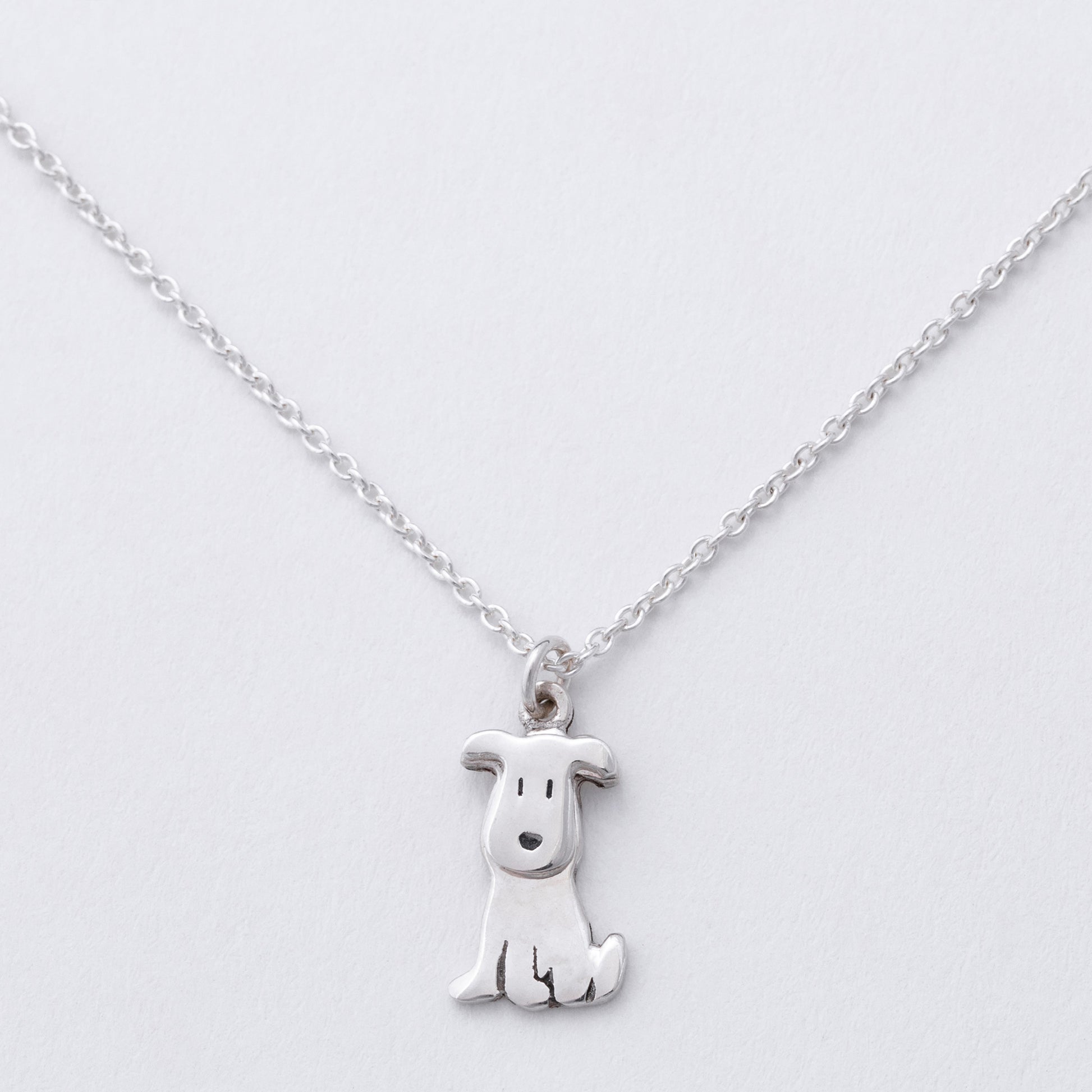 Silver dog-shaped pendant on a chain against a white background