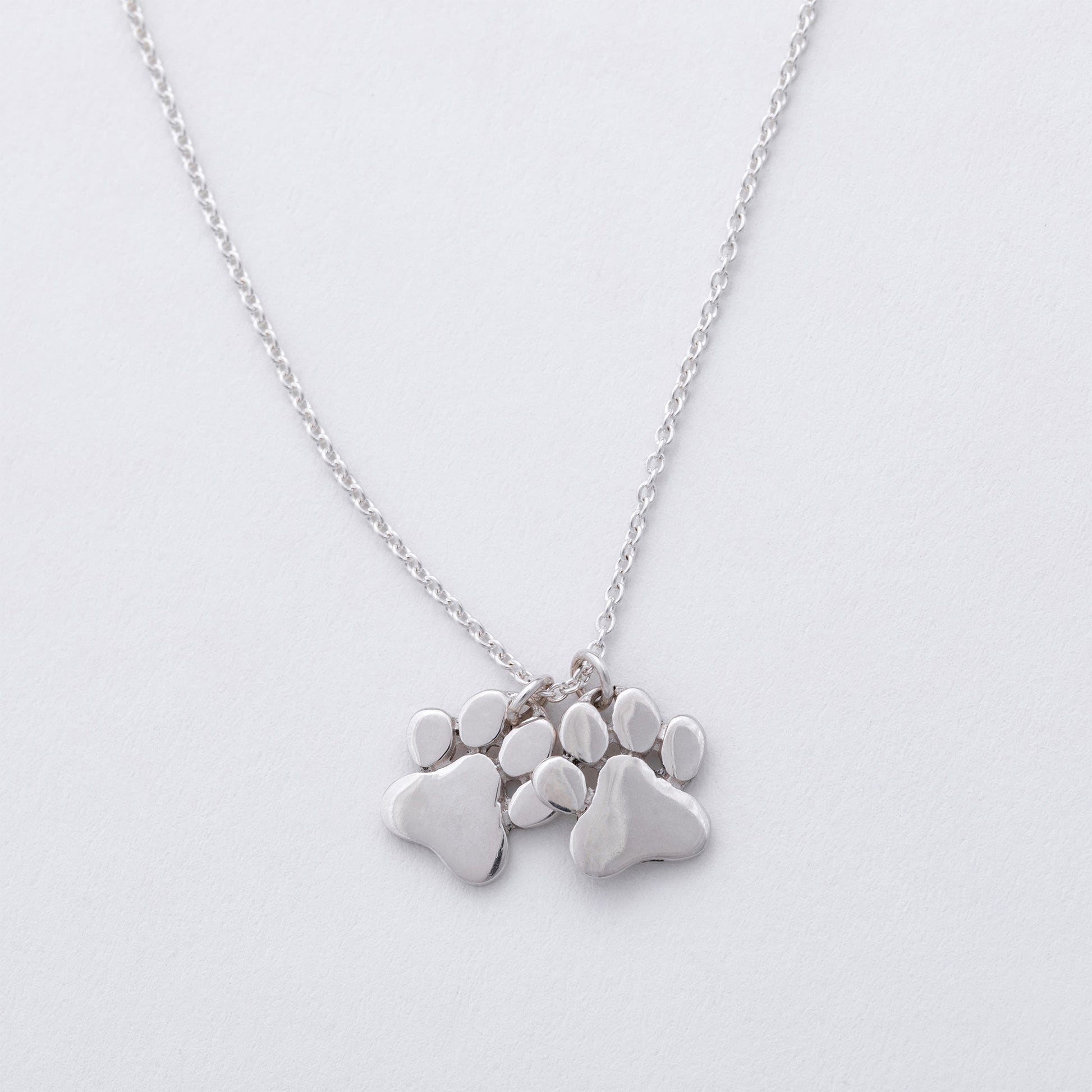 Silver necklace with paw-shaped pendants on a light gray background