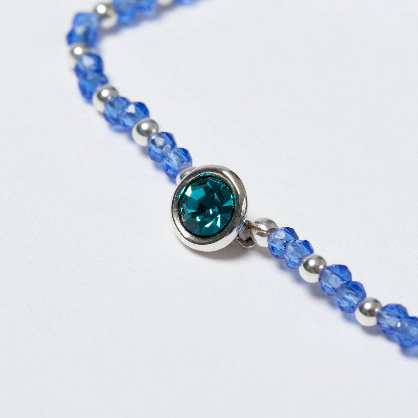 Bracelet with blue beads and a central teal gemstone on a white background