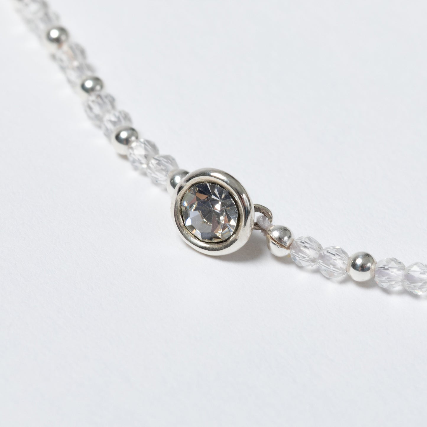 Close-up of a silver beaded necklace with a clear gemstone on a light gray background