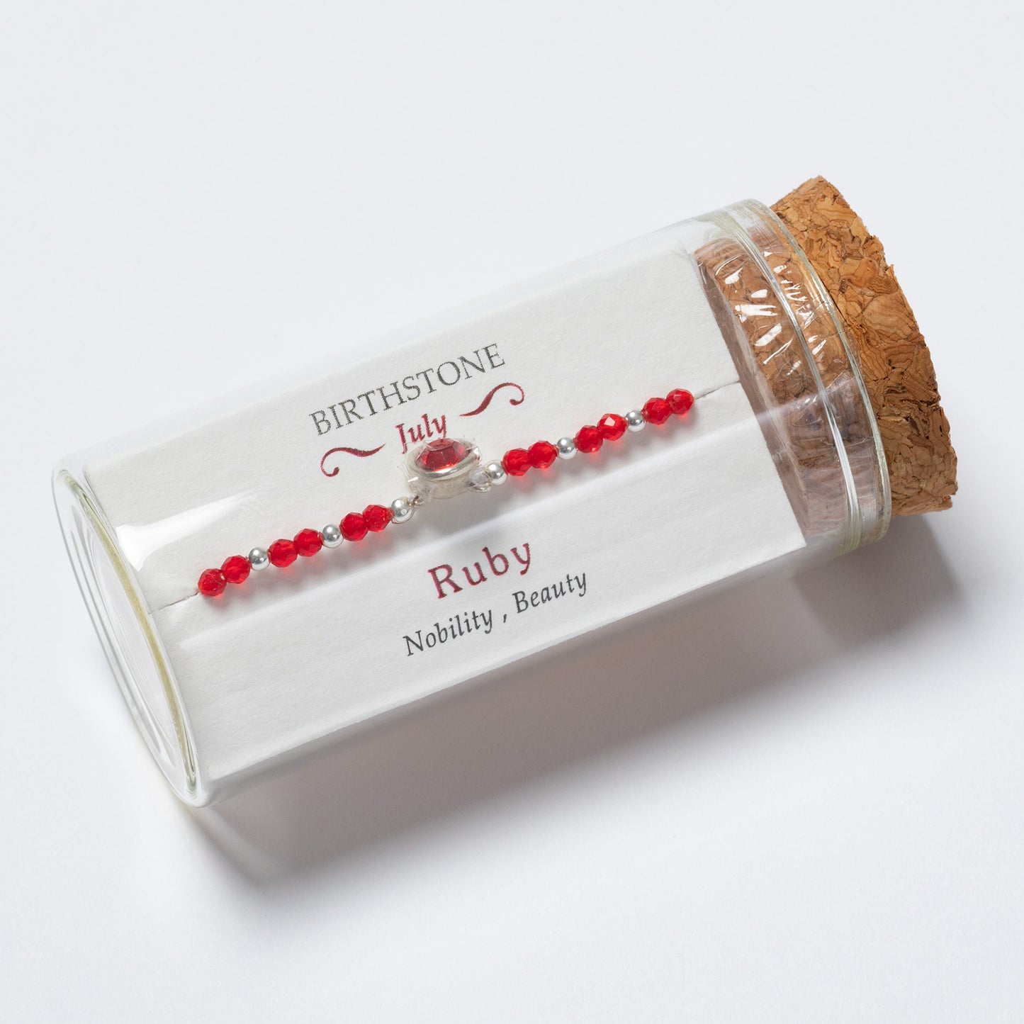 Ruby bracelet in a clear cylindrical box with cork lid on a white background