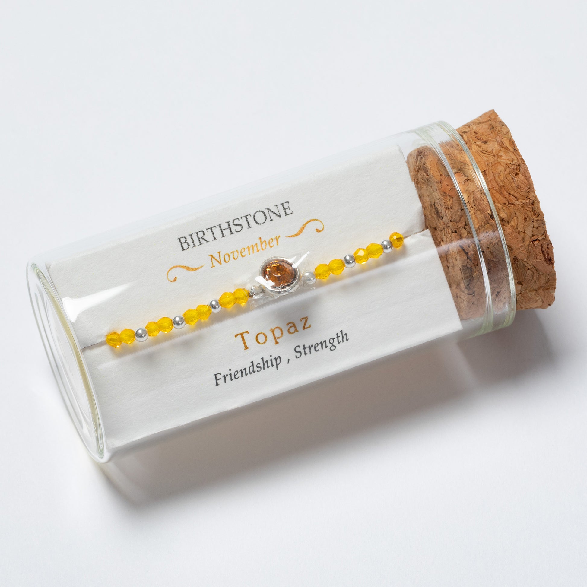 Topaz birthstone bracelet in a clear glass tube with cork lid on a white background