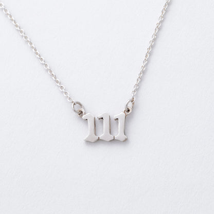 Silver necklace with a "111" pendant on a light gray background