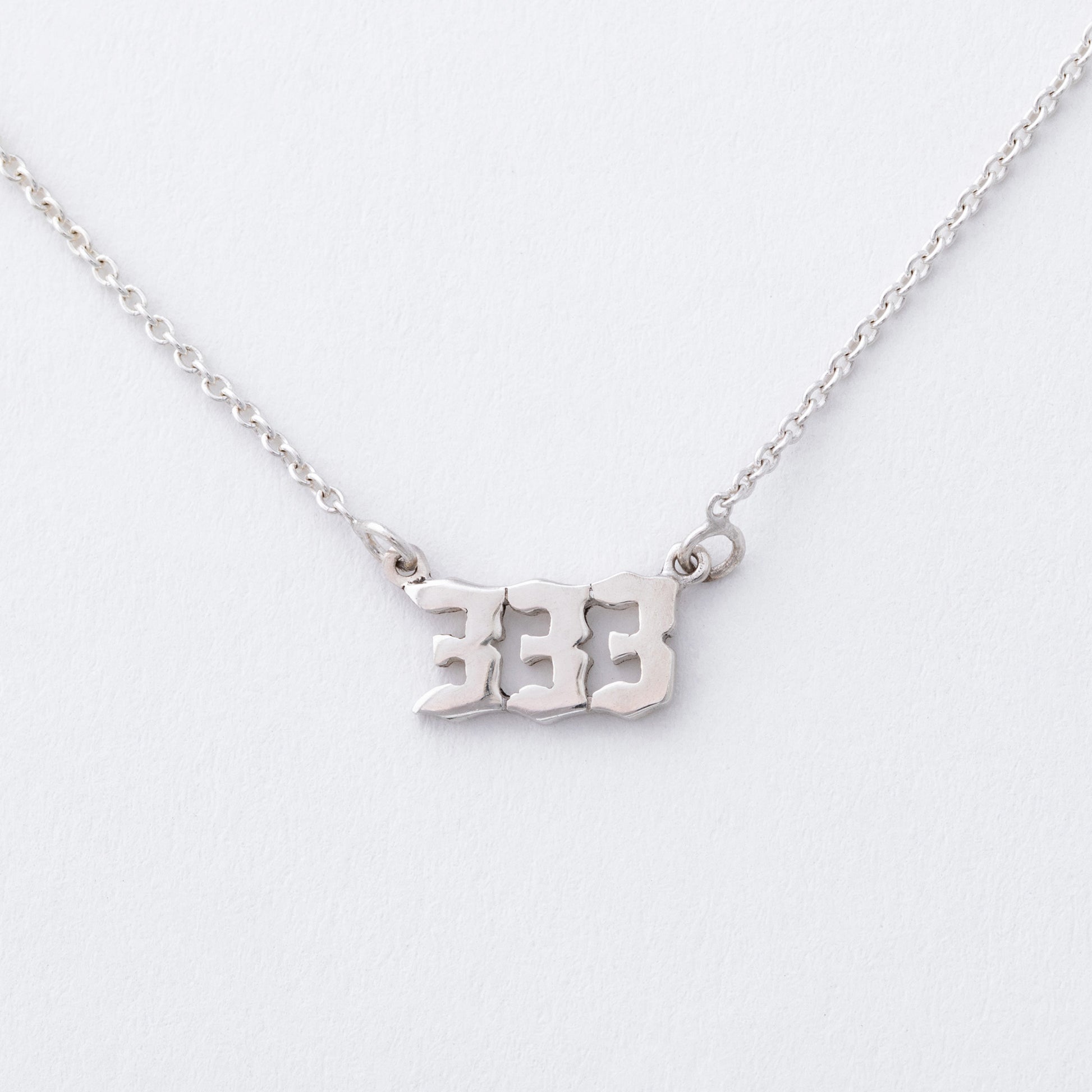 Silver necklace with '333' pendant on a white background