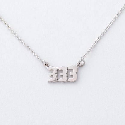 Silver necklace with '333' pendant on a white background