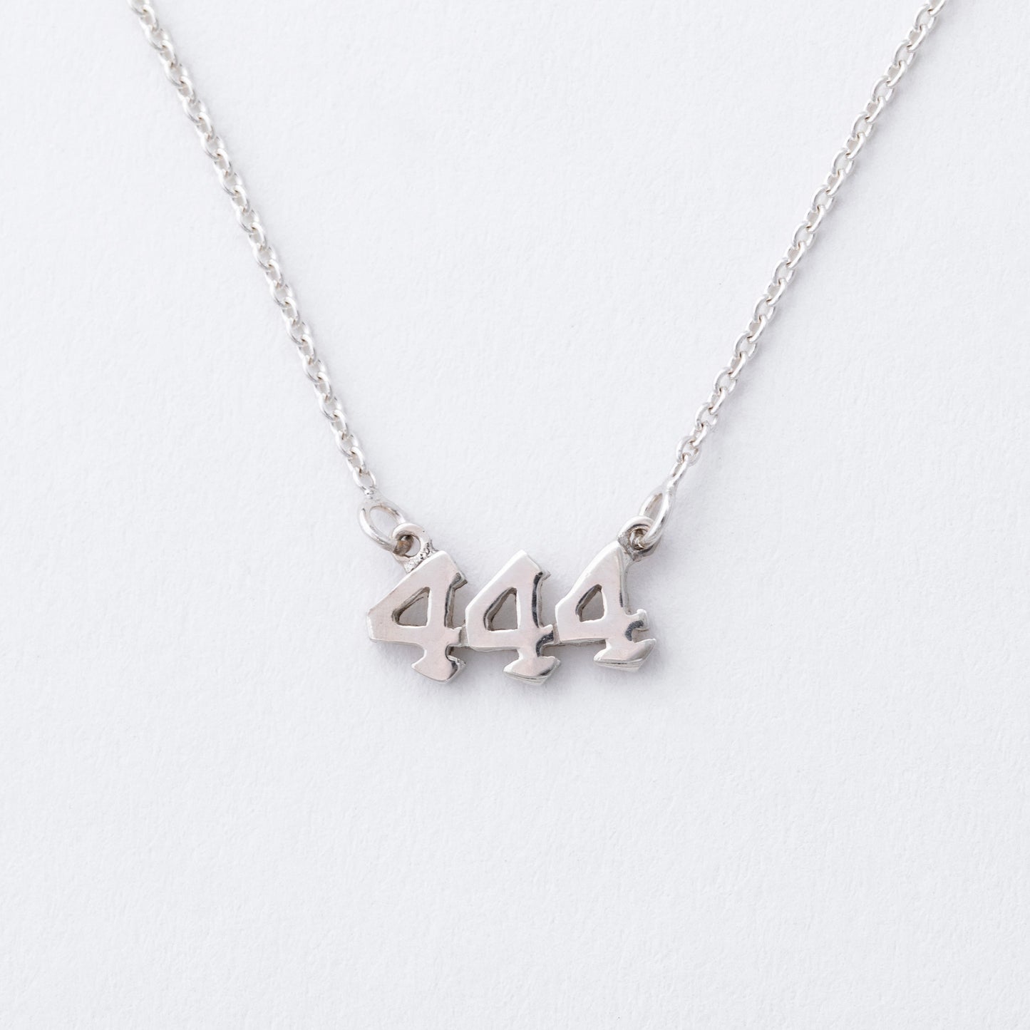 Silver necklace with '444' pendant on a white background