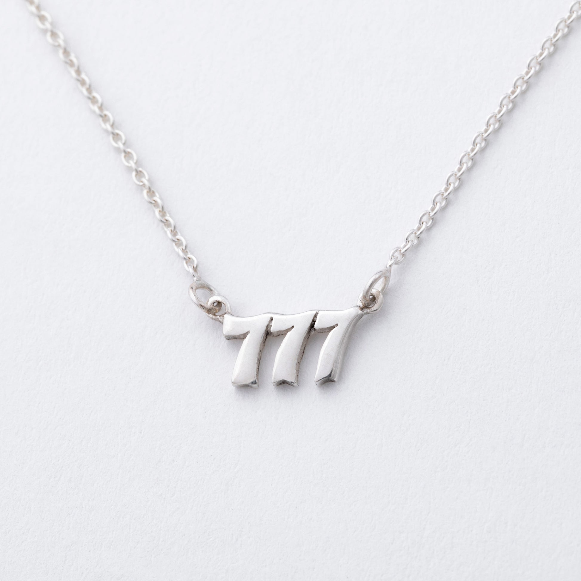 Silver necklace with the number '7' pendant on a light gray background