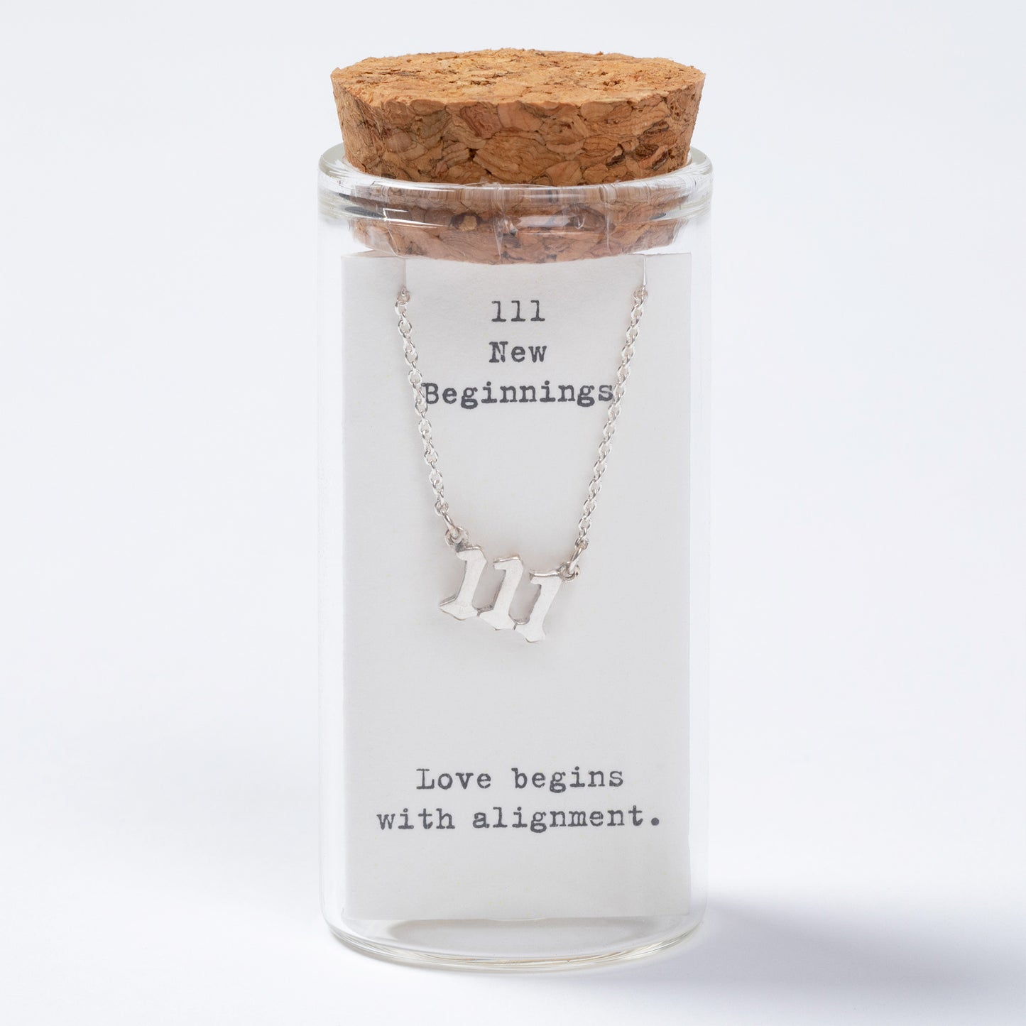 Glass jar with cork lid containing a necklace with 'III' symbol and text inside.