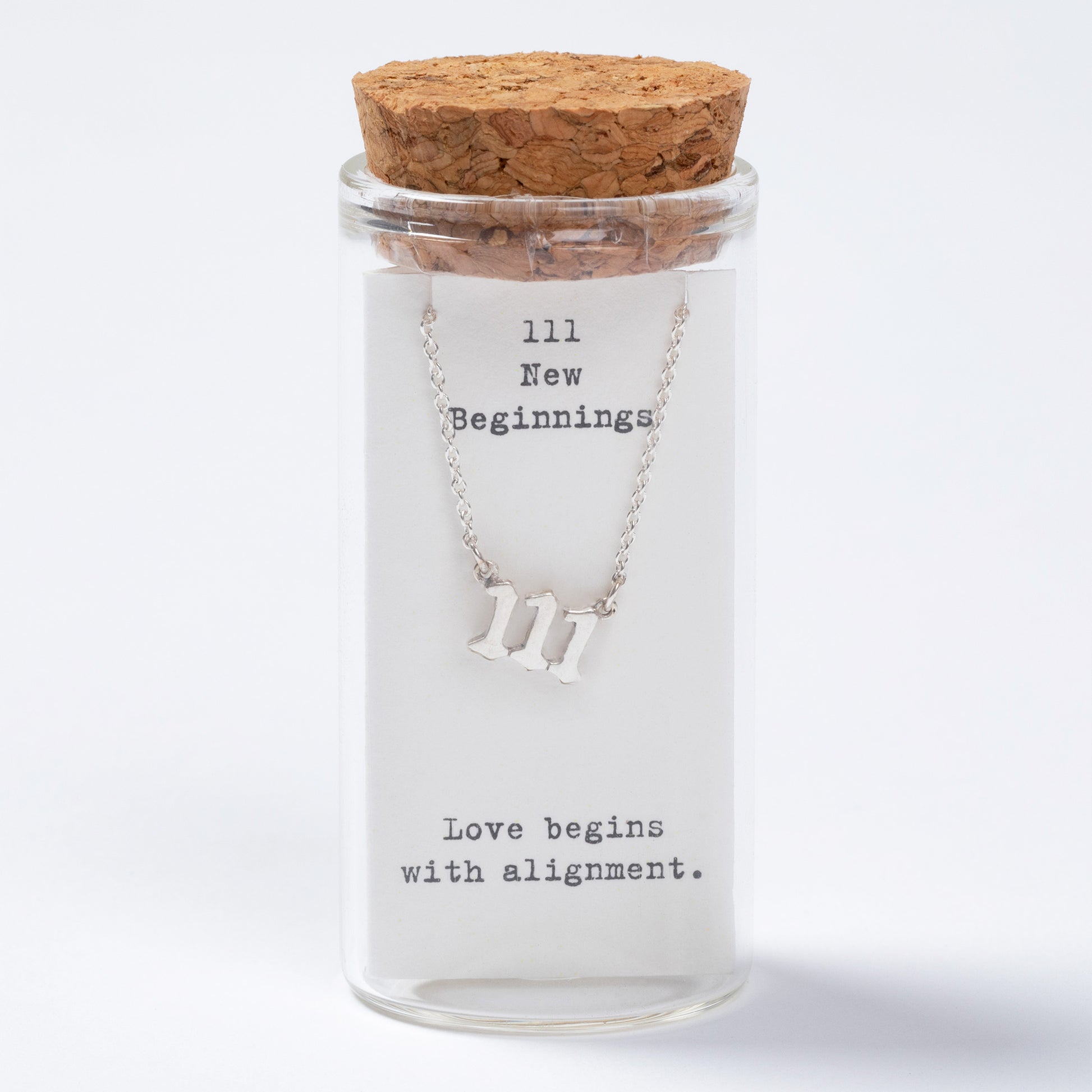 Glass jar with cork lid containing a necklace with 'III' symbol and text inside.