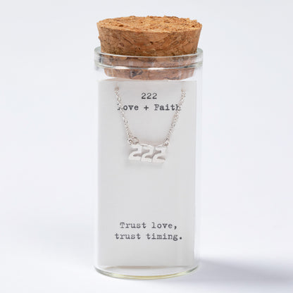 Glass jar with cork lid containing a necklace with '222' on a white background