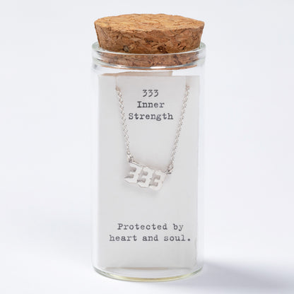 Glass jar with cork lid containing a necklace labeled '333 Inner Strength, Protected by heart and soul' on a white background