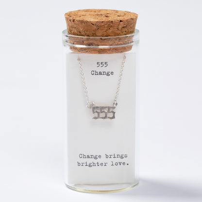 Glass jar with cork lid containing a necklace labeled '555 Change brings brighter love' on a white background