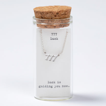 Glass jar with cork lid containing a necklace labeled '777 Luck' on a white background