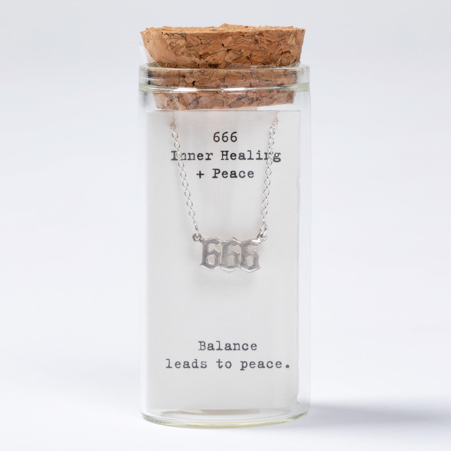 Glass jar with cork lid containing a necklace labeled '666 Inner Healing + Peace Balance leads to peace' on a white background.