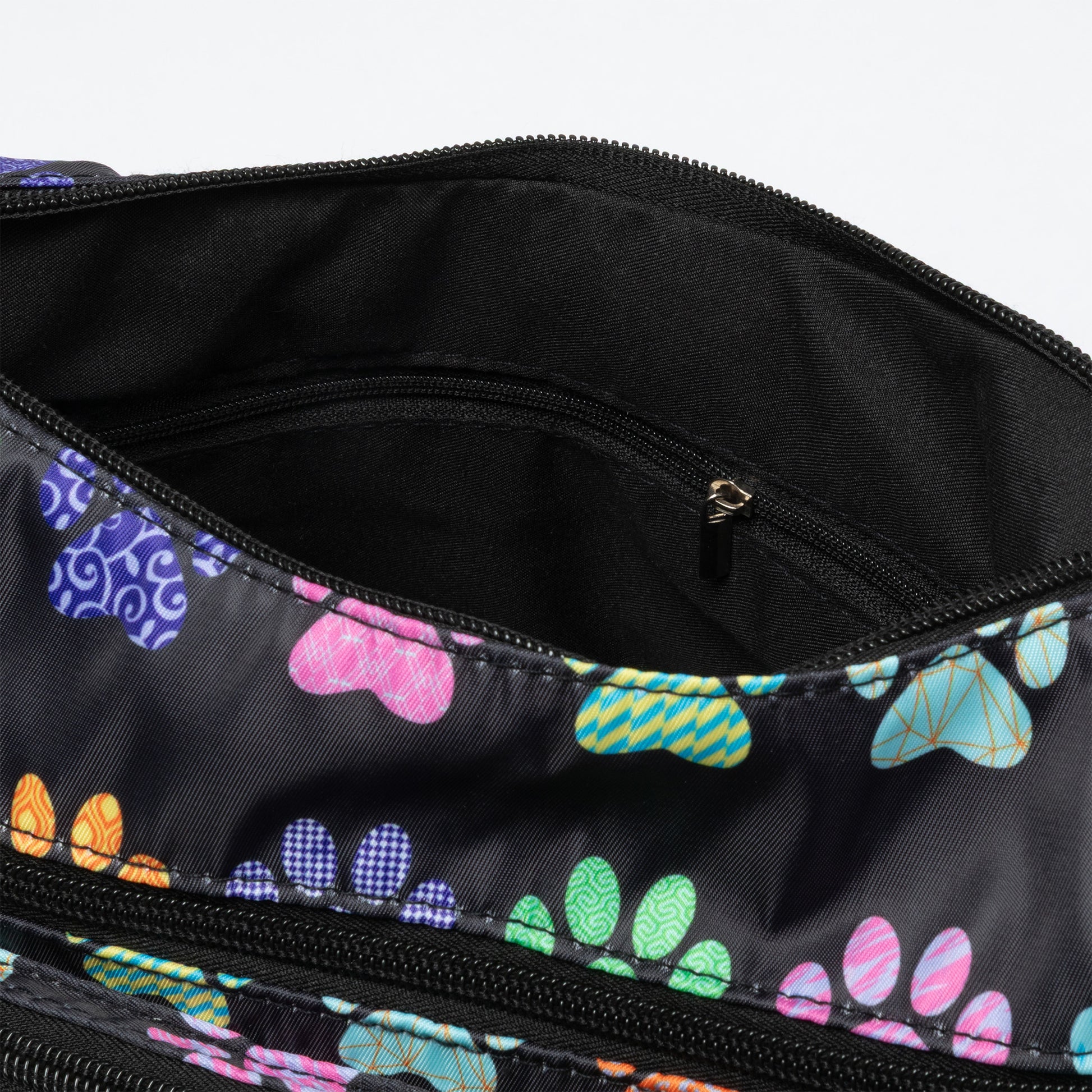 Close-up of the interior of a black zippered bag with a colorful paw print pattern lining, showing a black interior pocket with a small gold zipper pull.