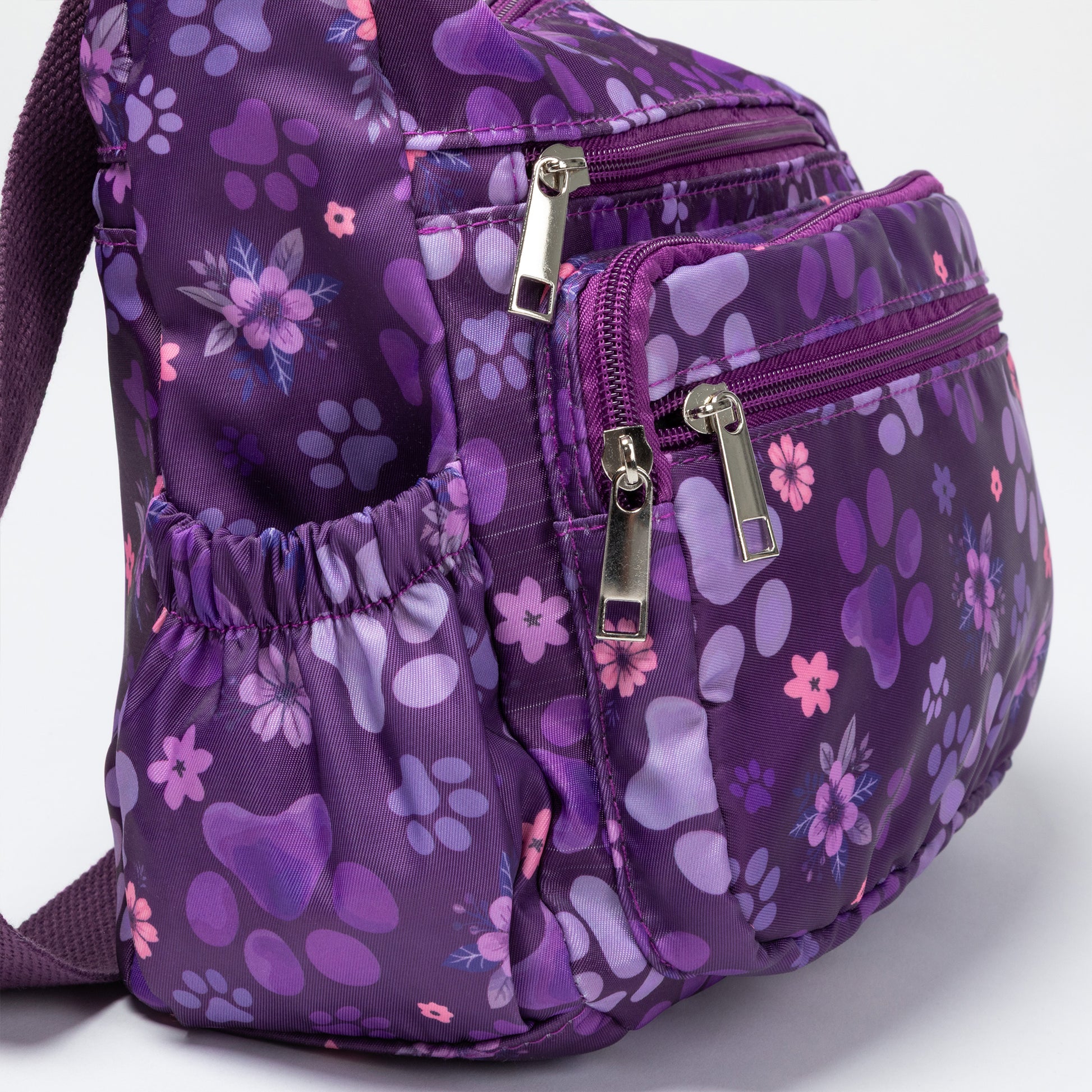 A purple nylon bag with a paw print and floral pattern, featuring multiple zippered compartments and a side pocket, photographed on a white background.