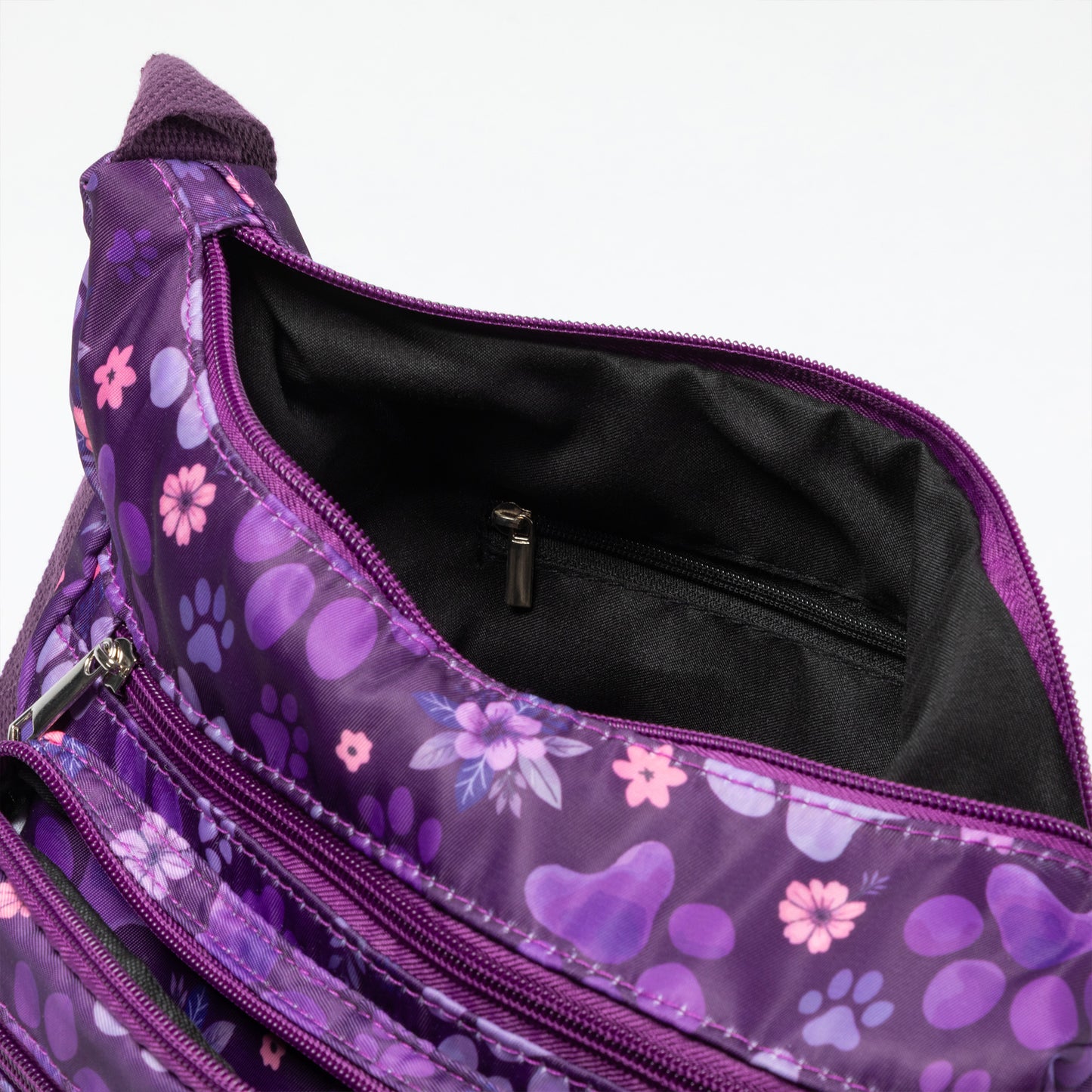 Close-up of a purple patterned bag with a floral and paw print design, showing the black interior lining and zipper compartments.