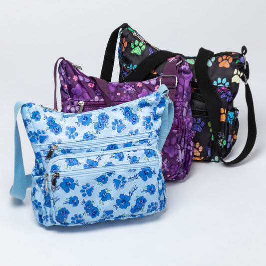 Three patterned crossbody bags arranged in a studio setting on a light gray background. The front bag is light blue with a blue floral print and a light blue strap.