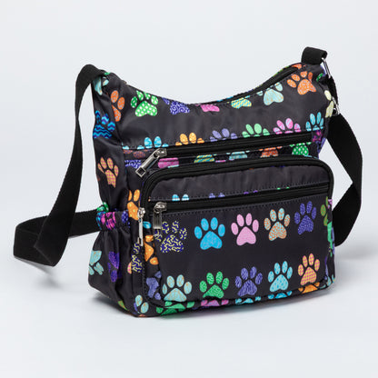 A black crossbody bag with a colorful paw print pattern, featuring multiple zippered compartments and a black shoulder strap, photographed on a light gray background.