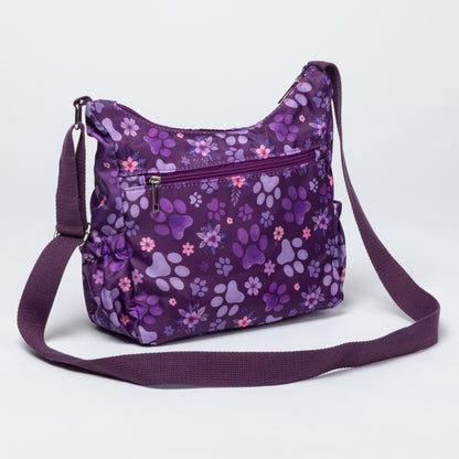 A purple crossbody bag with a floral and paw-print pattern, featuring multiple zippered pockets and a matching adjustable shoulder strap, shown on a light gray background.