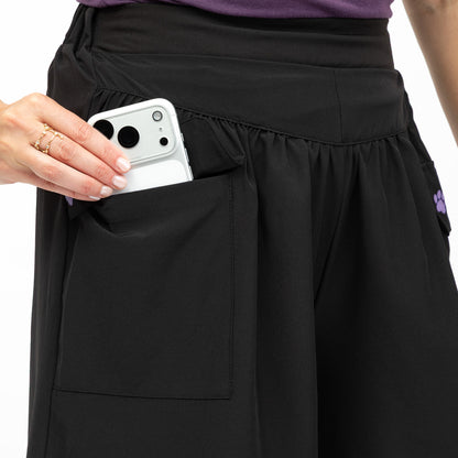 Person wearing black shorts with a pocket, holding a white phone.