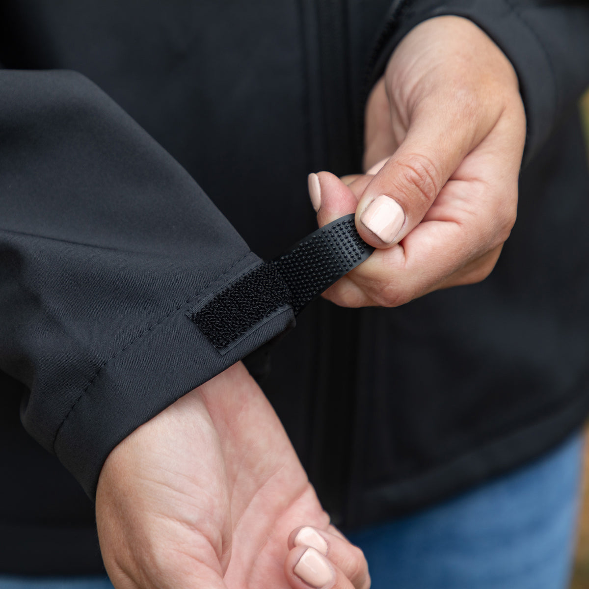 Close-up of a person's hands fastening a black hook-and-loop strap on the cuff of a black jacket.