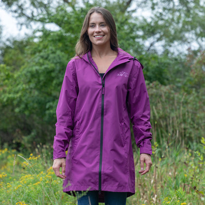 A woman wearing a purple hooded raincoat with a black front zipper, standing outdoors in a grassy field with trees in the background.