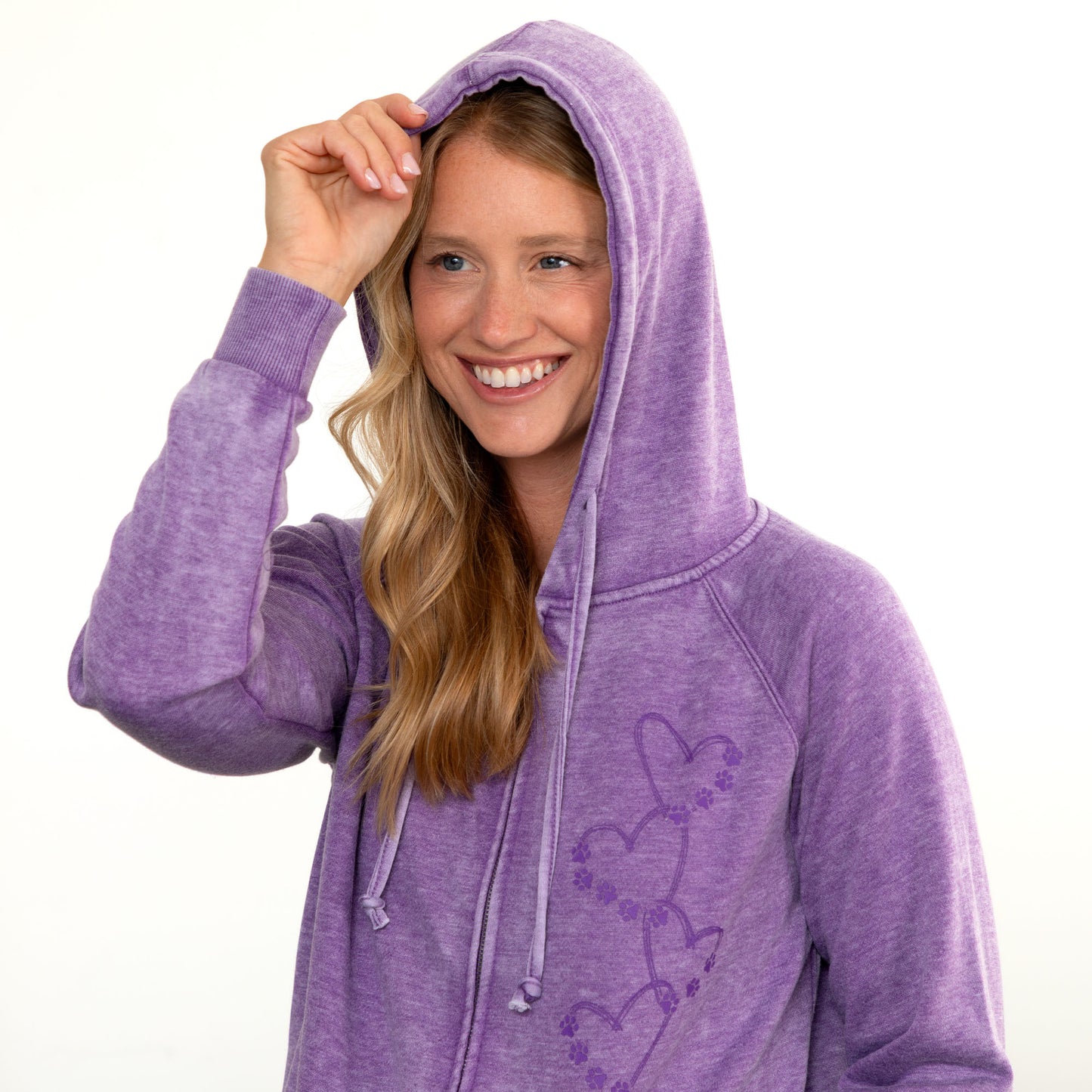 A smiling woman wearing a lavender purple heathered zip-up hoodie with a tonal heart graphic on the front, posed against a solid white background.