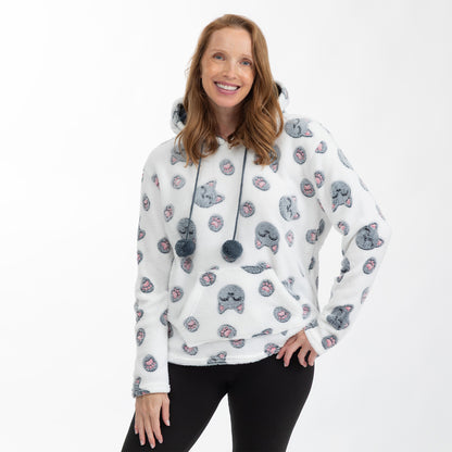 A woman wearing a white sherpa hoodie with a repeating pattern of gray cartoon cats with pink paw prints, paired with black leggings, against a plain white background.