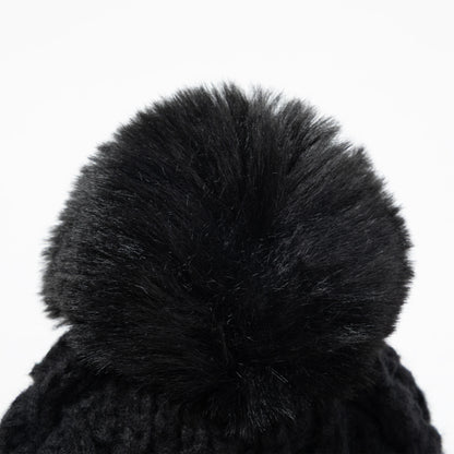 Close-up of a black knit beanie with a large fluffy faux-fur pom-pom on a plain white background.