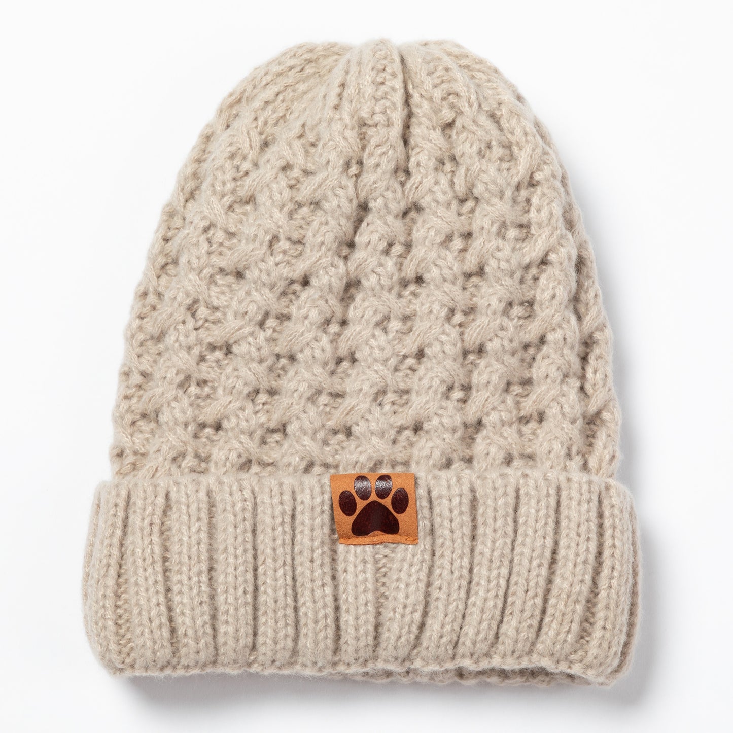 A beige cable-knit beanie hat with a folded cuff and a small brown paw-print patch on the front, shown against a plain white background.