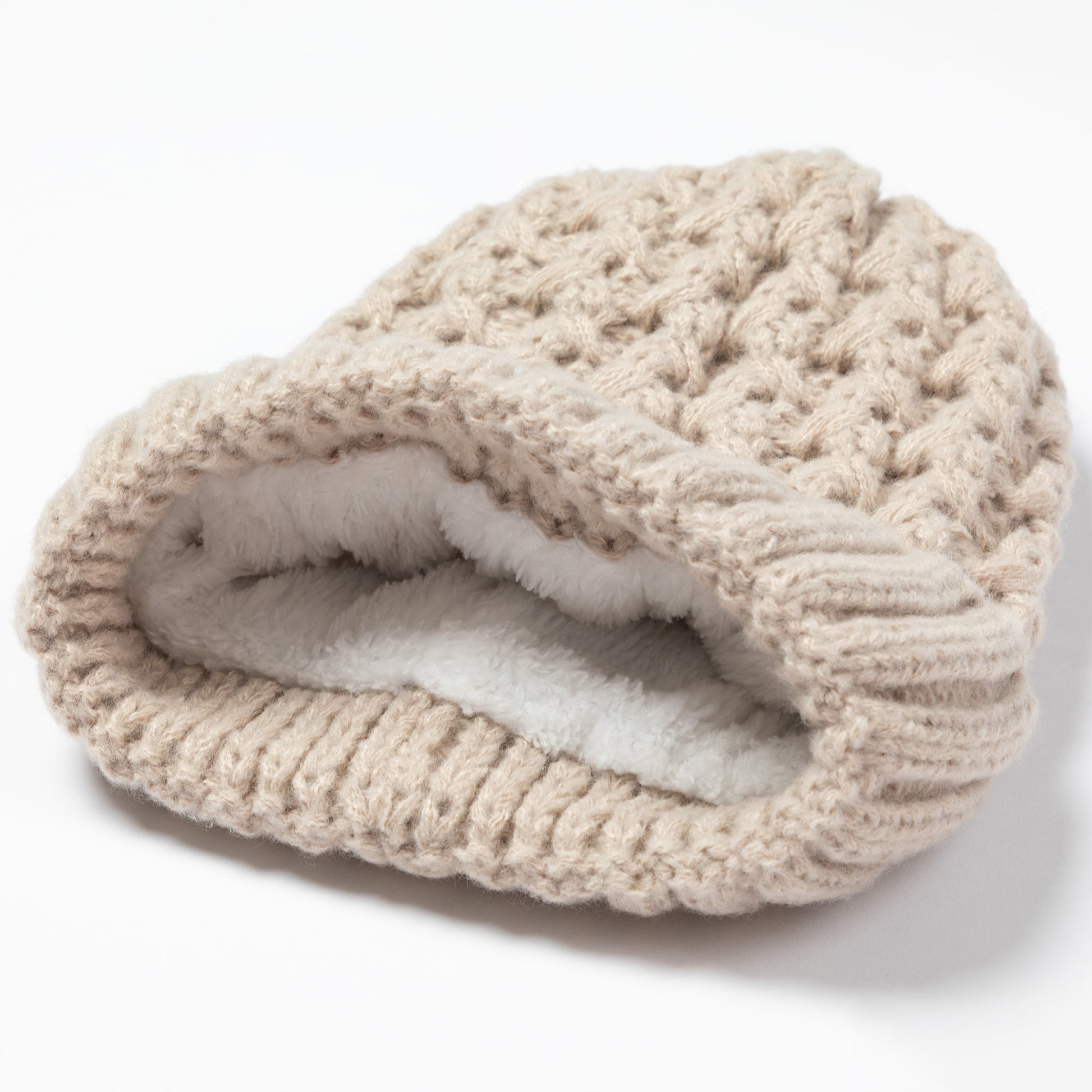 A chunky knit beanie hat in a warm beige color, featuring a thick white faux-fur lining visible inside the folded opening, set against a plain white background.