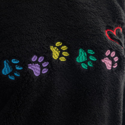 Close-up of a black fuzzy fabric with embroidered colorful paw prints and a red heart.