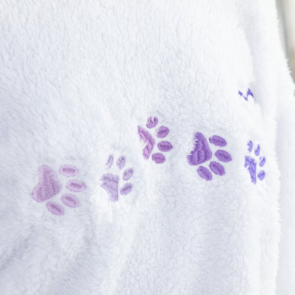 Close-up of a white plush fabric with embroidered purple paw prints running horizontally across it.