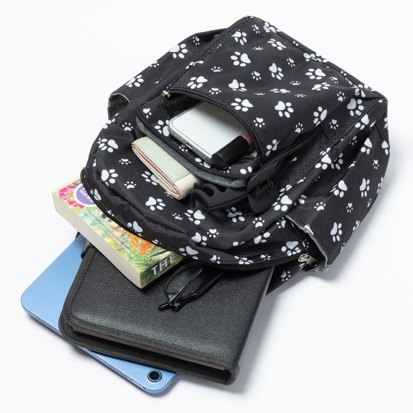 A black backpack with a white paw print pattern, shown open and filled with various items including a tablet, wallet, and books, on a clean white background.