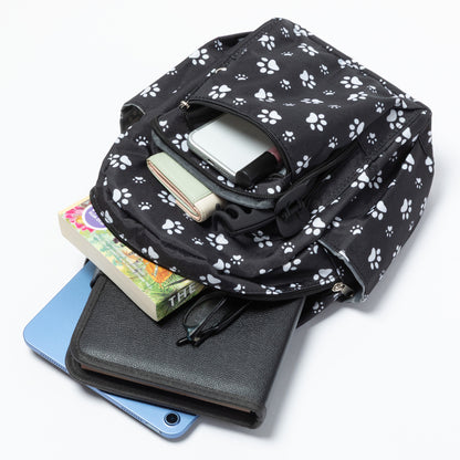 A black backpack with a white paw print pattern, shown open and filled with various items including a tablet, wallet, and books, on a clean white background.