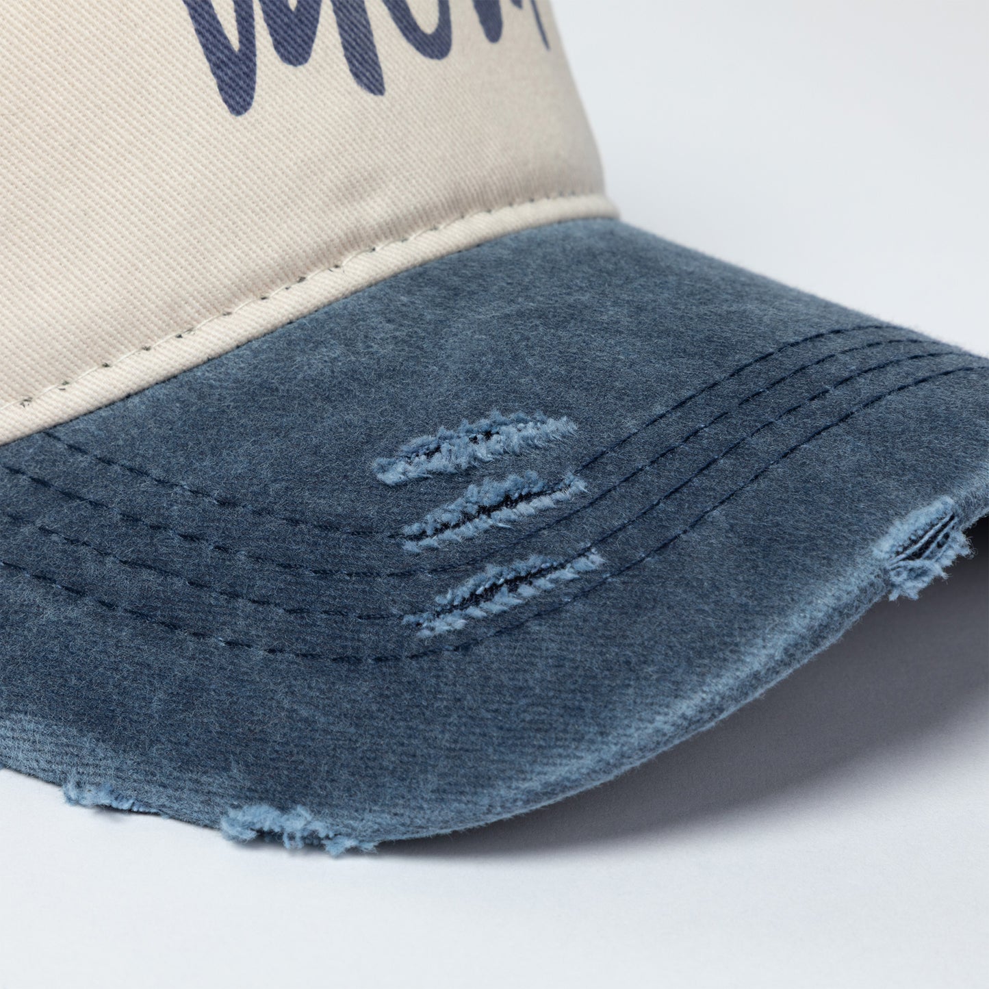 Trucker hat with distressed denim brim and beige top on a light gray background