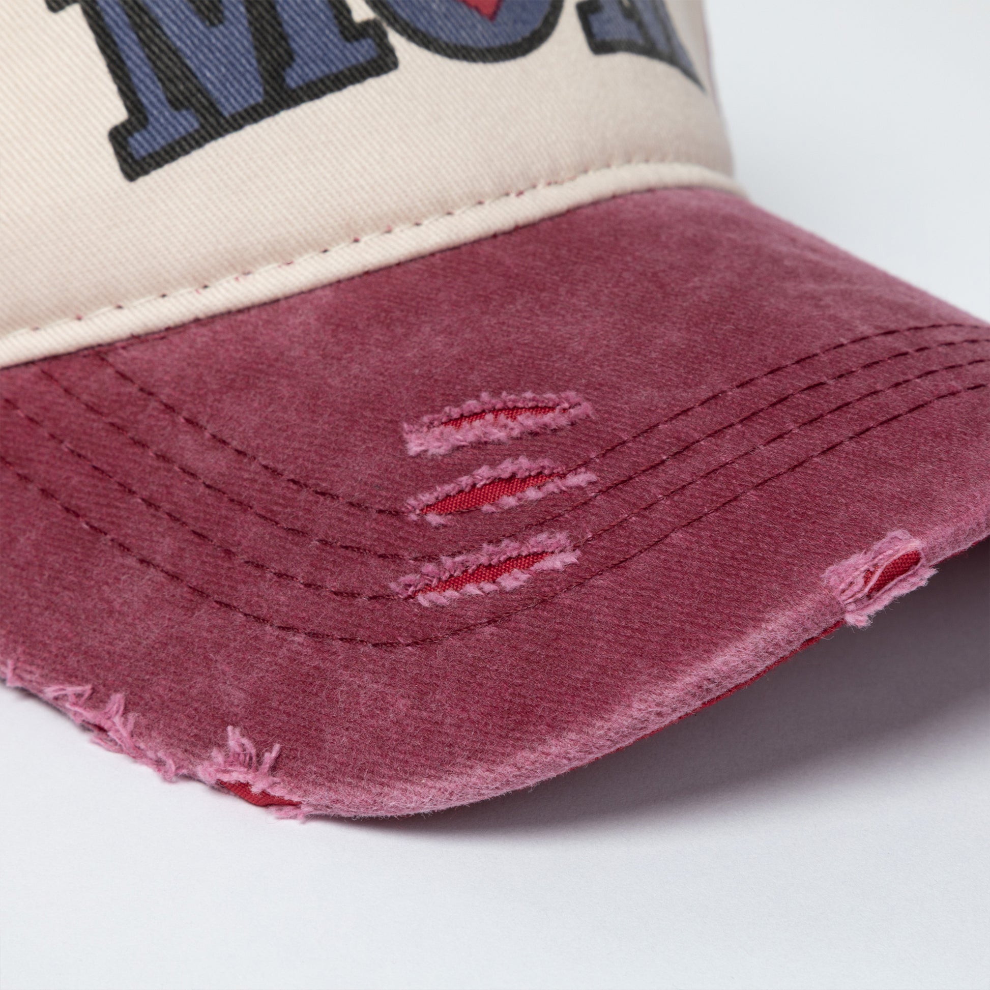 Close-up of a distressed baseball cap with a white and red design on a light gray background