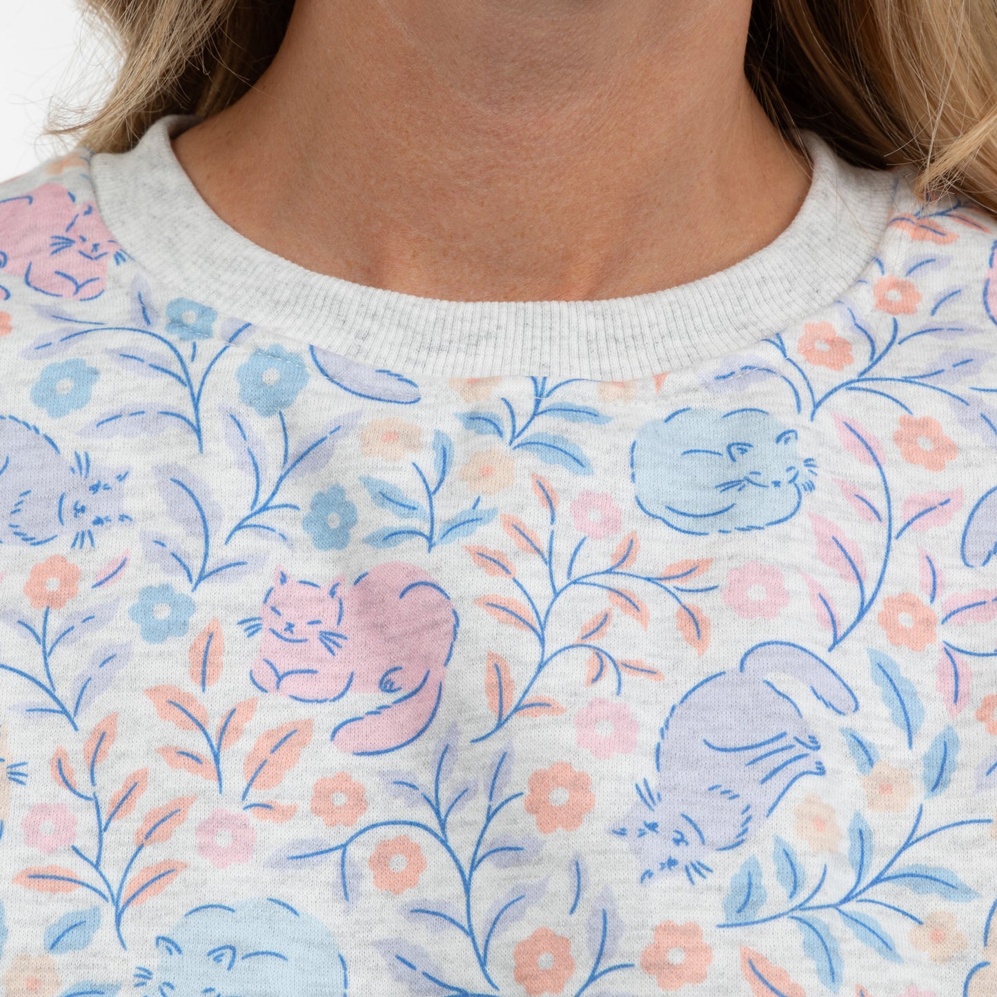 Close-up of a person wearing a light gray crewneck sweatshirt with a pastel cat and floral pattern.