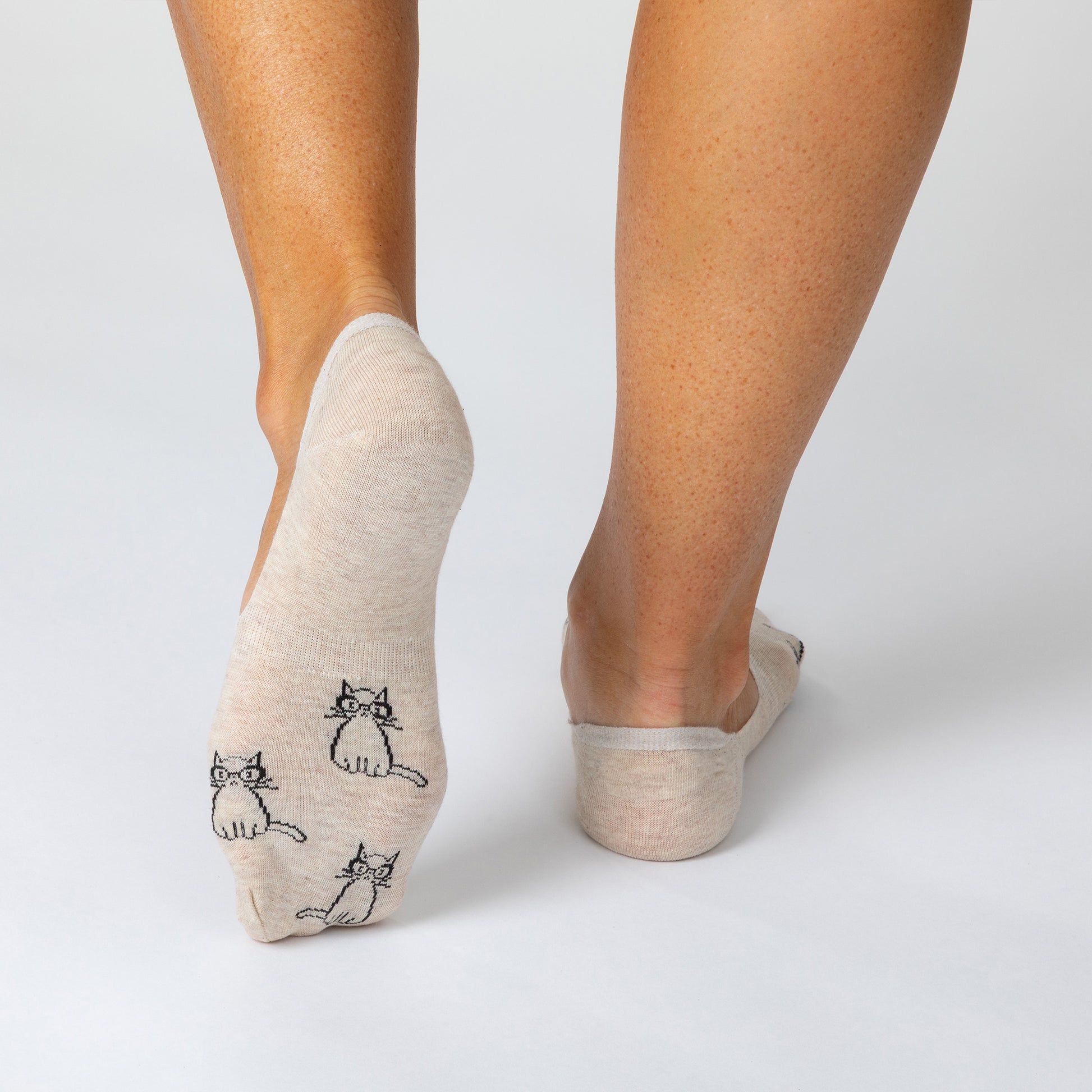 Beige socks with cat designs worn by a person on a light gray background