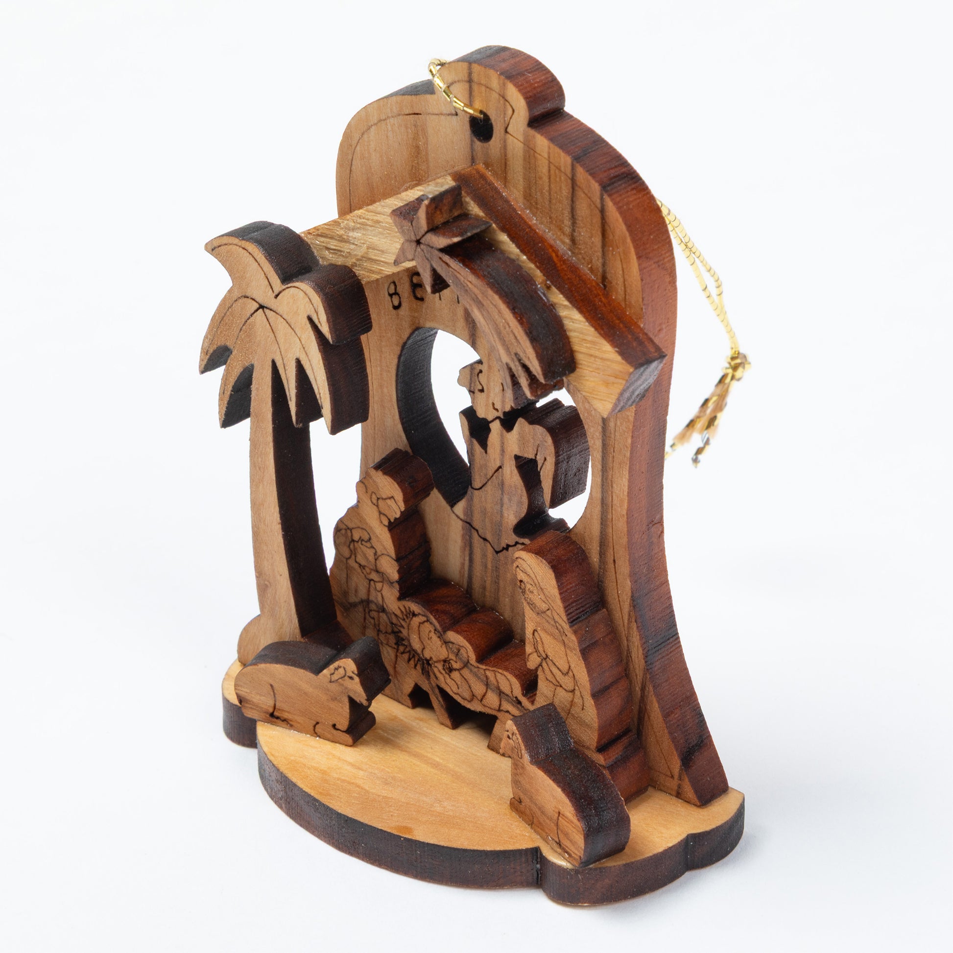 A handcrafted wooden nativity scene ornament featuring carved figures, a palm tree, and a stable structure, shown on a clean white background.