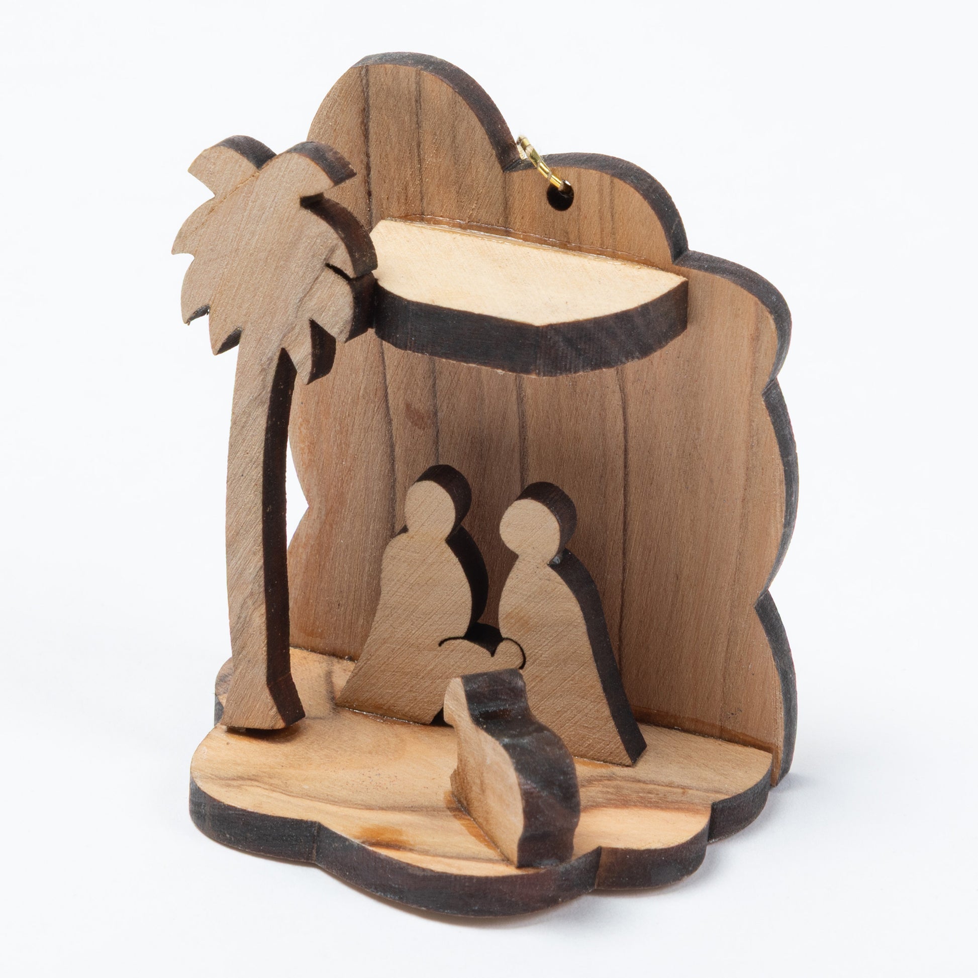 A small wooden nativity scene ornament featuring a palm tree, stable backdrop, and silhouettes of Mary, Joseph, and baby Jesus, photographed on a plain white background.