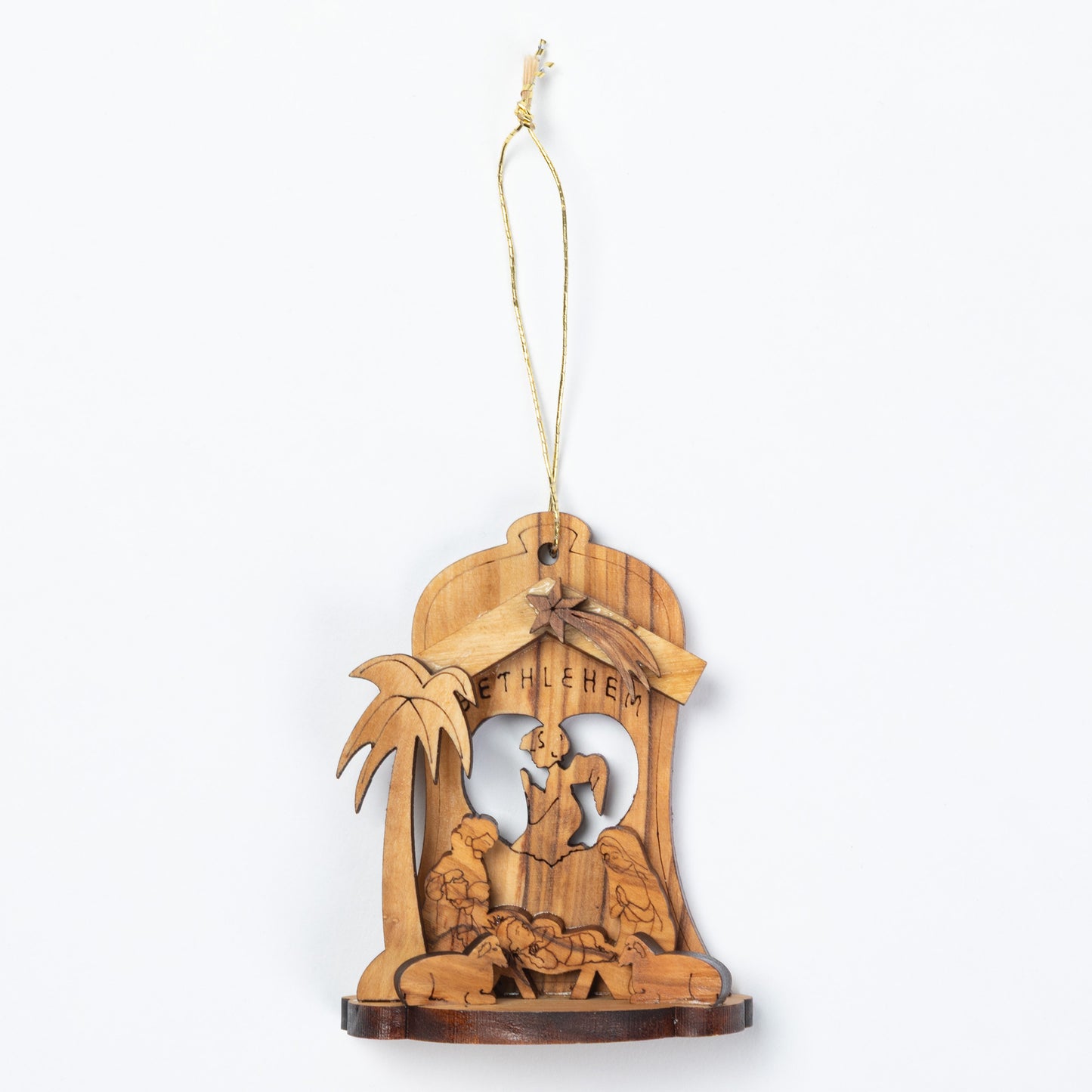 A handcrafted wooden nativity ornament featuring a carved stable scene with a palm tree and the word 'BETHLEHEM' on a light wood background, suspended by a thin string.