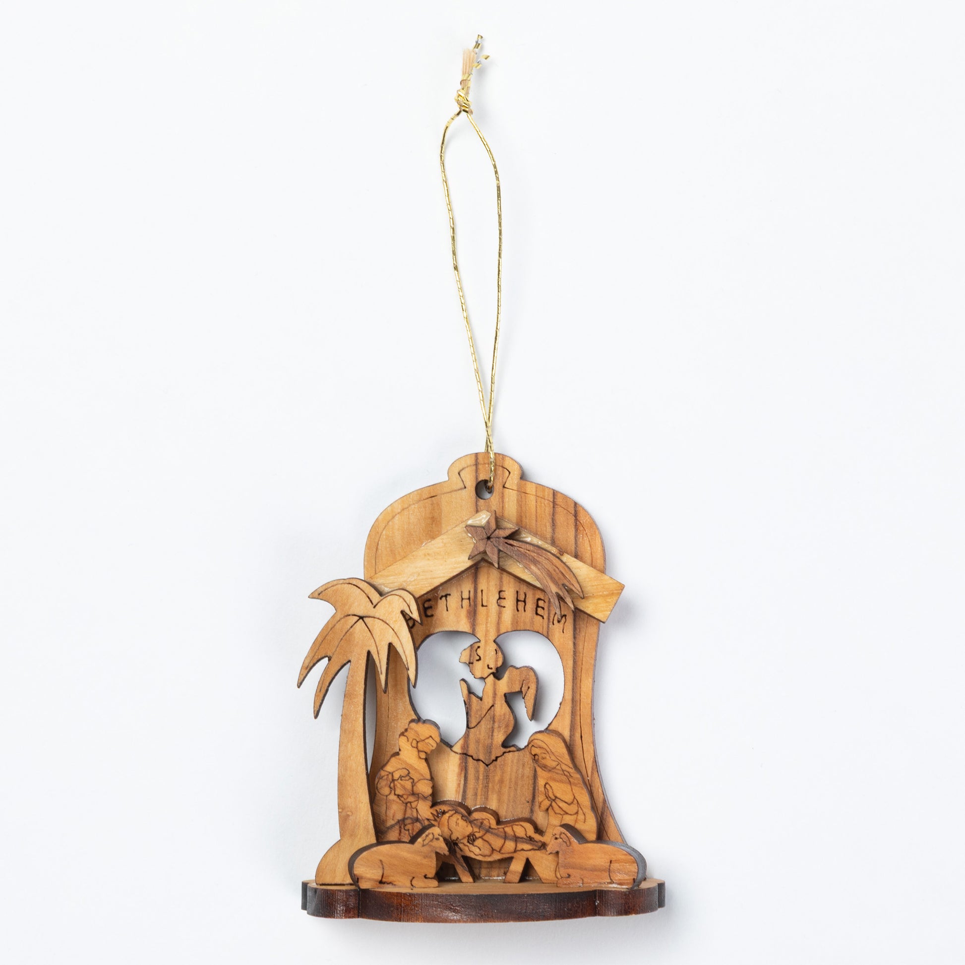 A handcrafted wooden nativity ornament featuring a carved stable scene with a palm tree and the word 'BETHLEHEM' on a light wood background, suspended by a thin string.