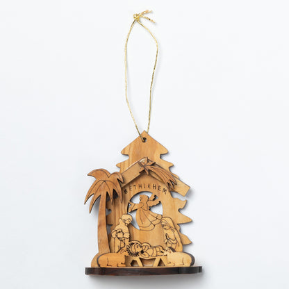 A wooden Bethlehem nativity ornament hanging from a gold string, featuring laser-cut scenes of the Holy Family, a palm tree, and a dark wood base on a white background.