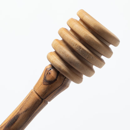 A close-up of a wooden honey dipper with a ribbed spiral head and a smooth handle, shown against a plain white background.